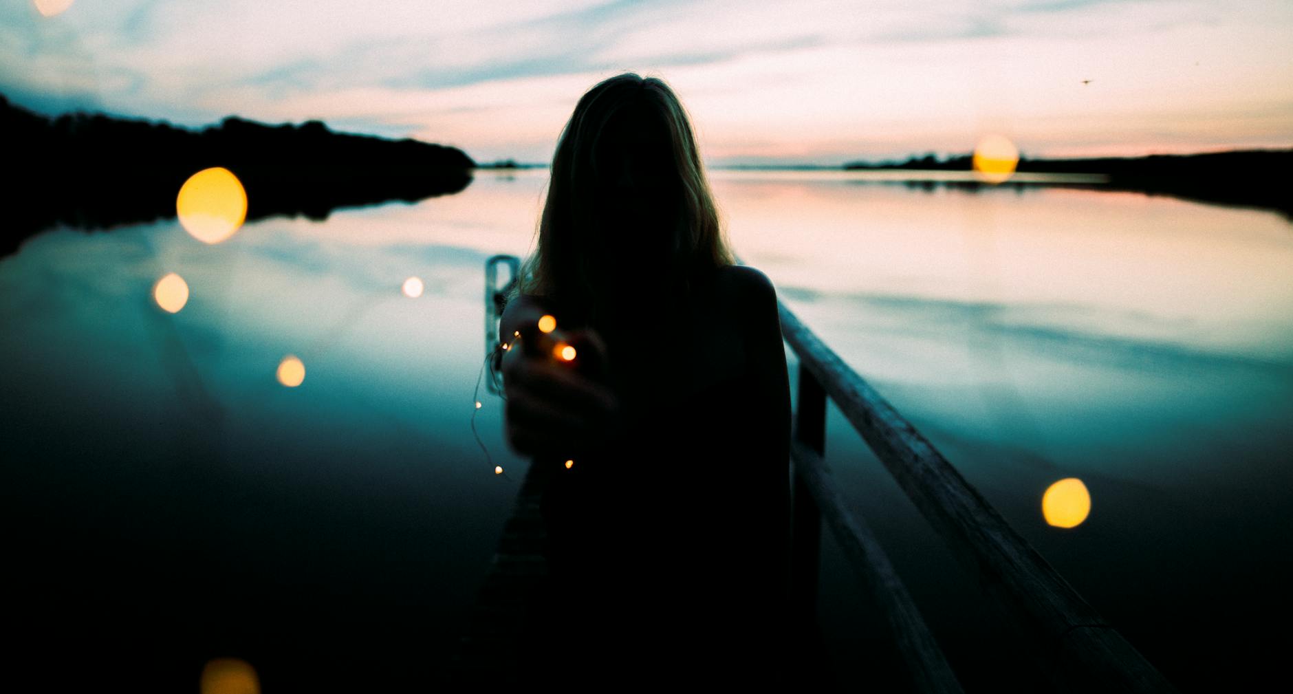 silhouette of woman leaning on metal railings with background of body of water by the shoreline